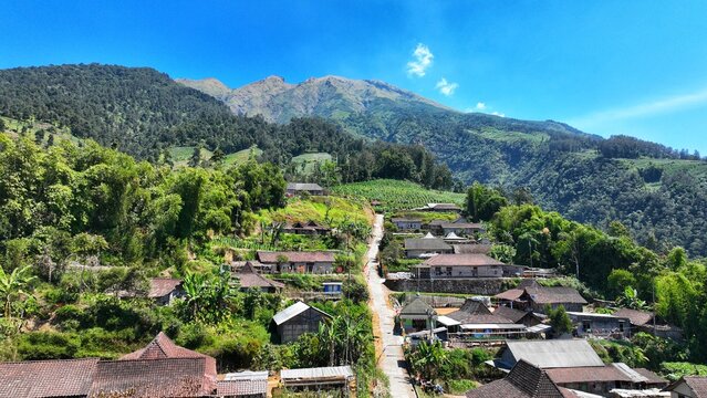 Aerial view of KEMA MERBABU Glamour Camping nestled among village houses and lush green hills with Mount Merbabu in the background in Kecamatan Ampel, Jawa Tengah, Indonesia.
