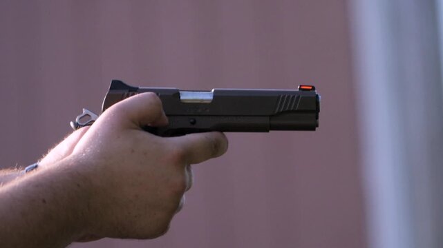 Close-up side view of a shooter firing a 1911-style pistol, capturing recoil, slide movement, and rising gun smoke in dramatic slow motion.