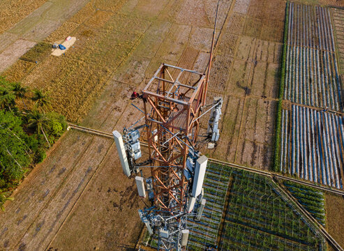 Aerial view of a telecommunications tower standing amidst agricultural fields and rural landscape in Patikraja, Central Java, Indonesia.