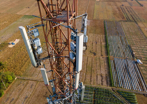 Aerial view of a telecommunications tower with antennas rising above agricultural fields and rural farmland, Patikraja, Central Java, Indonesia.