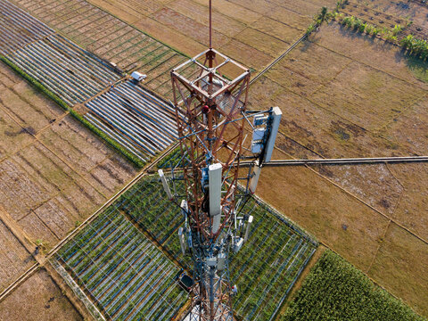 Aerial view of a telecommunications tower standing amidst agricultural fields and irrigation patterns in Patikraja, Central Java, Indonesia.