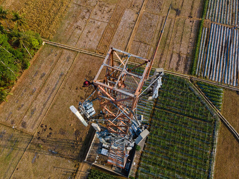 Aerial view of a telecommunications tower standing amidst agricultural fields and rural landscape in Patikraja, Central Java, Indonesia.