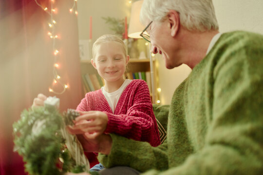 Caucasian senior man and granddaughter decorating holiday wreath together. Concept representing family bonding, suitable for winter marketing campaigns