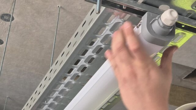 Slow motion cinematic close up of fixing an industrial neon light to the underside of a cable tray.