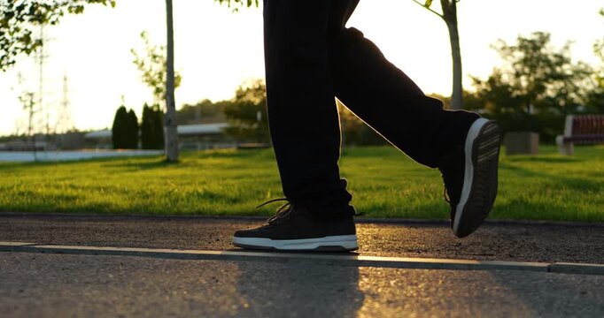 Child walks through green park at sunset. Schoolboy steps along paved path in warm golden light, representing active childhood, outdoor recreation, healthy habits, freedom and youthful energy.