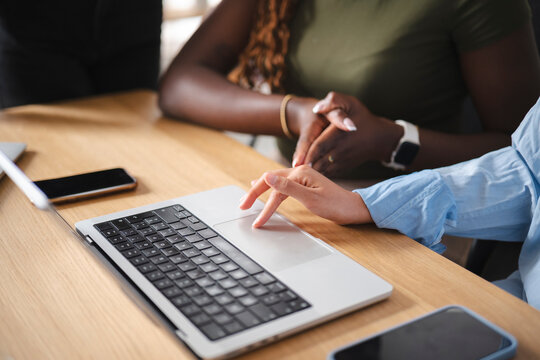 Two diverse female colleagues work together in a bright modern office. One woman types on a laptop while her coworker watches closely during a collaborative project meeting.