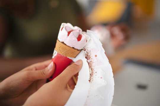 A person holds a delicious strawberry ice cream cone, carefully peeling away the paper wrapper to enjoy the sweet dessert during a sunny afternoon break indoors.