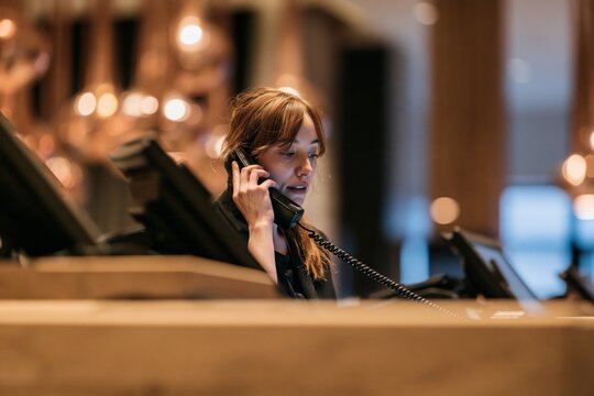 Receptionist talking on a telephone at a hotel front desk with warm ambient lighting in lobby