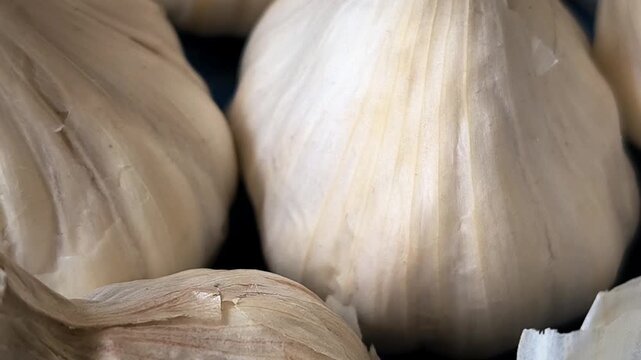 A smooth, slow camera pan from right to left showcasing macro details of fresh whole garlic bulbs with dry papery skin. Perfect for cooking channels, healthy food concepts, culinary videos