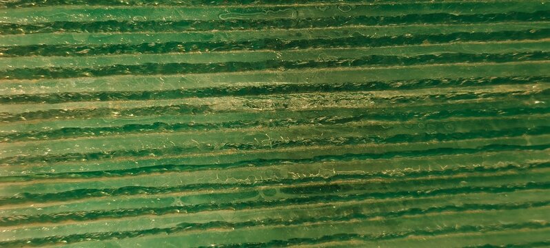 A macro shot of a glossy green material featuring parallel horizontal ridges with subtle irregularities. The translucent surface reflects light across its grooves, creating a detailed abstract pattern