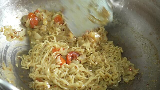 Cooking instant noodles with onions and tomatoes in a pan
