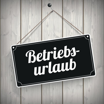 Schwarzes Schild an der Holzwand mit dem Wort Betriebsurlaub