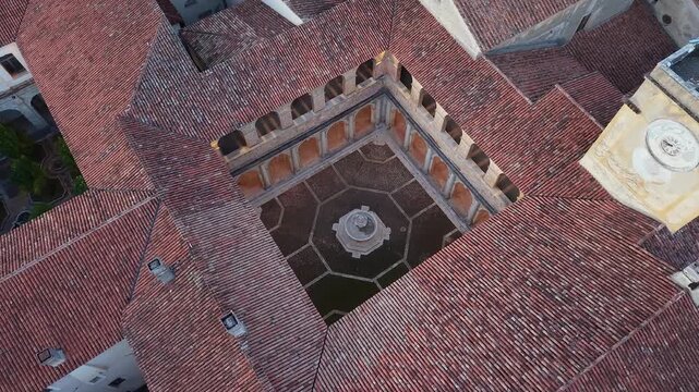 Aerial top down view of a cloister with a stone fountain surrounded by terracotta roofs at the Charterhouse of Padula, Campania, Italy