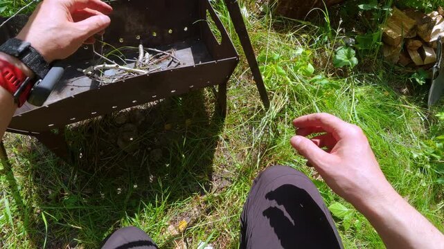 POV of man putting small dry branches and twigs into portable grill to start campfire