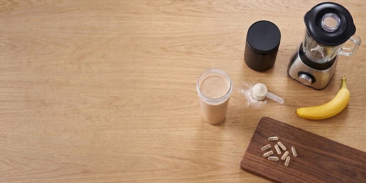 Sports supplements, shaker and banana arranged on wooden table for workout nutrition. Concept of fitness products, pre-workout nutrition and active lifestyle content.