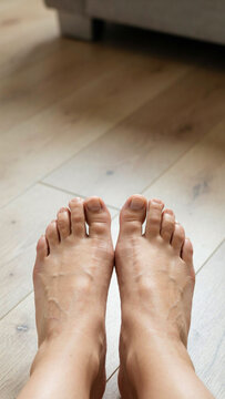 Close-up of bare human feet on a light-colored wooden floor with hardwood standing interior perspective wellness podiatry dermatology domestic lifestyle movement toenails structure