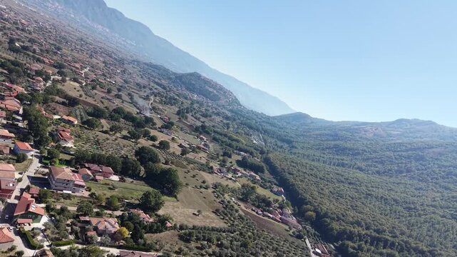 Rotating aerial view of a hillside village among olive groves above the Vallo di Diano valley, Cilento National Park, Campania, Italy