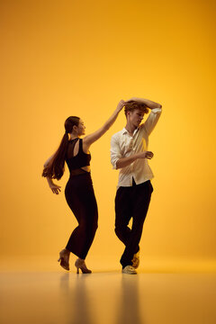 Bachata leader guides partner through energetic turn in orange studio with joyful rhythm. Latin choreography, dynamic motion and partner trust concept.