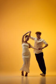 Graceful bachata woman turns beneath partner arm in orange studio with poised confidence. Underarm turn, partner guidance and Latin dance concept.