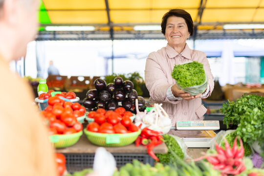 Smiling elderly female seller telling prices for fresh vegetables at local bazaar