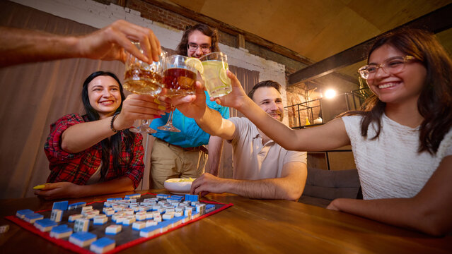 Joyful friends toast above Mahjong tiles after successful round at home. Shared victory, friendly competition and game night concept.