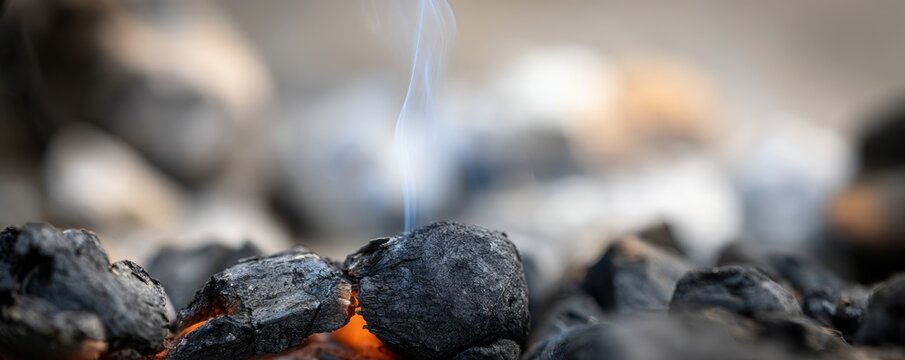 Glowing hot charcoal briquettes in a barbecue grill with rising blue smoke