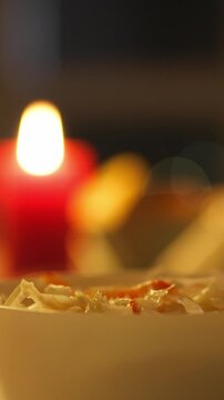 A diner holding chopsticks consumes noodles from a bowl during an evening restaurant meal, enjoying food in a dimly lit dining space with warm ambiance and close atmosphere
