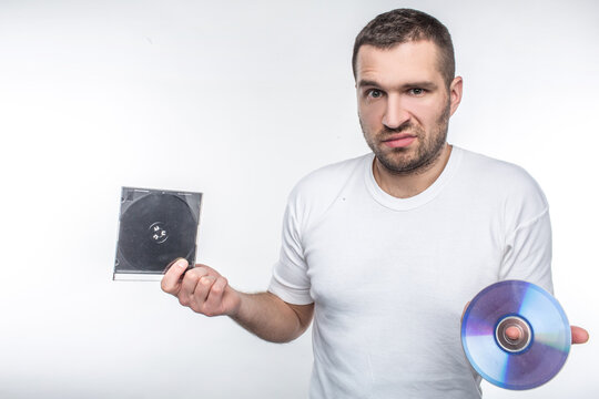 Young man holding a compact disk in one hand and a box from it in another hand and staring at camera. Time goes so fast that now he doesn't know what to do with this disk. Isolated on white.