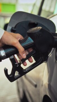 A female hand grips a fuel nozzle, placing it into the vehicle gas tank at an active fuel station. The pumping procedure starts, providing necessary energy for ongoing transportation