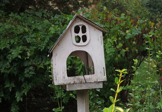 House-shaped bird house on a post on green bushes background
