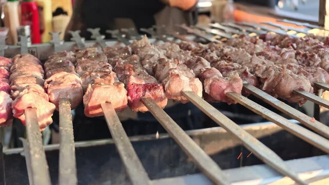 SLOW MOTION: hand of chef turning rows of authentic Italian arrosticini lamb skewers cooking on a smoking charcoal grill, preparing a popular street food from the Abruzzo region in Italy