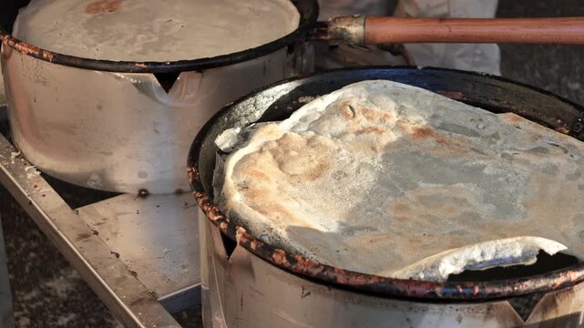 Chef in orange gloves frying multiple borlengo crepes on large pans, preparing traditional Emilia-Romagna street food often served with grated Parmigiano Reggiano cheese in Italy SLOW MOTION