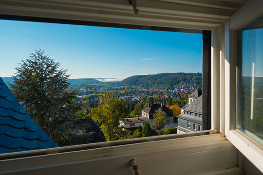 Alte Holzfenster im Fachwerkhaus mit tollem Fernblick &uuml;ber die Stadt mit Wald und H&auml;usern am Tage bei Sonne