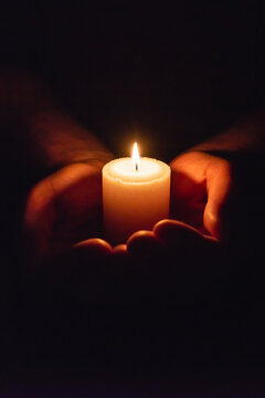 Person holding burning candle in the dark with vertical copy space for remembrance and hope.