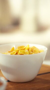 A wooden table holds a bowl filled with crunchy breakfast flakes and a glass of fresh milk, presenting a simple morning nutrition scene with natural light on a daily meal setup