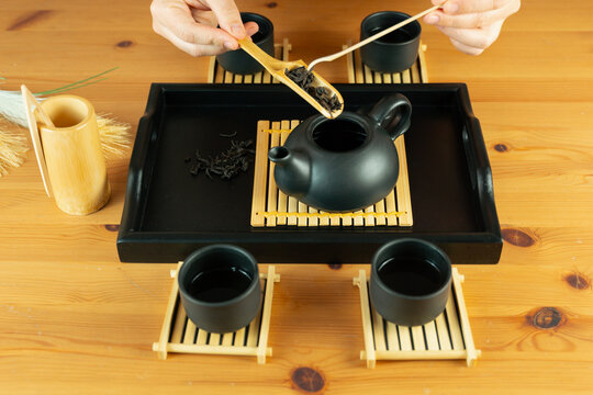 chinese tea ceremony hands putting dry tea leaves from bamboo chahe into chahu teapot, gongfu tea set with pinming cups on chaban tray and wooden table concept of tea culture, restaurant, relaxation