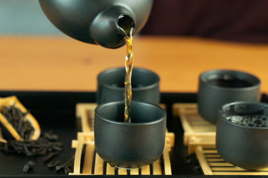 chinese tea ceremony gongfu tea set black ceramic chahu teapot pouring tea into pinming cups on bamboo coasters, dry leaves in chahe scoop on chaban tray concept of tea culture, restaurant, relaxation