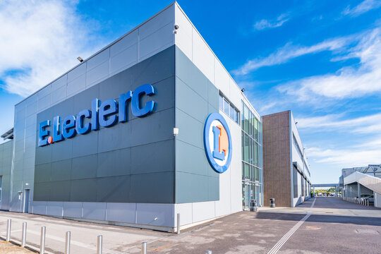 Exterior of an E.Leclerc hypermarket in Incarville, Eure, Normandy, showing the large blue lettering, the circular logo and the glass entrance under a bright blue sky.