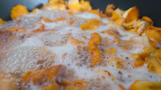 Orange mushrooms boiling in foamy water with bubbles rising around sliced caps and stems during closeup cooking process in dark pan