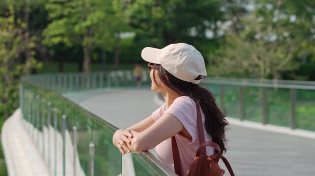 Happy young Asian woman relaxing and walking along the walkway enjoying freedom in green city park