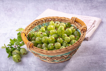 Grey stone surface with woven wicker basket filled with green gooseberries, fresh summer berry harvest © Andrei Starostin