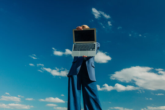 Businesswoman in formal blue suit with laptop against blue sky, low angle view