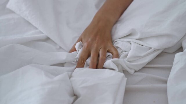 Sensual woman gripping sheets in private moment.