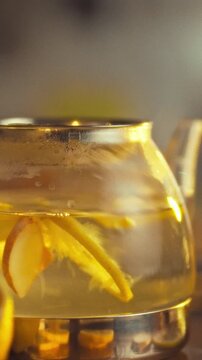 Close-up view of lemons and ginger swirling inside a glass teapot on a kitchen counter with utensils and sliced citrus, capturing the beverage preparation and cooking process
