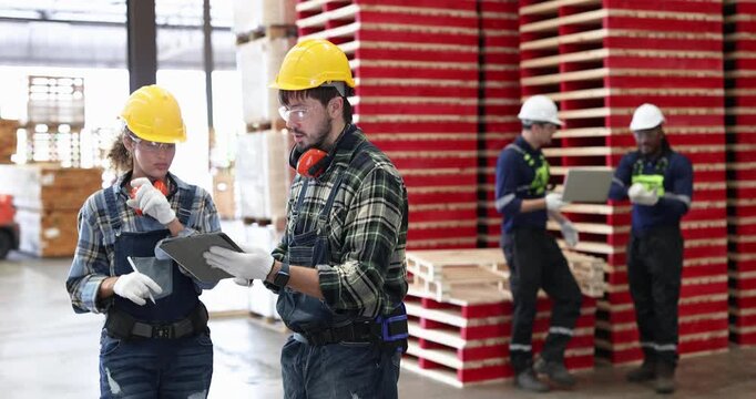 Workers discussing tasks in a warehouse with wooden pallets stacked in the background
