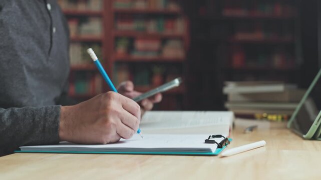 Student engaged in study conducts online study sessions, takes study notes with pencil, manages research data, performs academic research indoors.