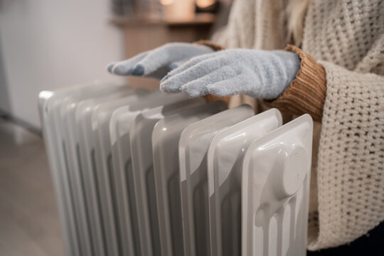 very cold inside home with heating problems. Woman sitting trying to warm up by their electric heater.