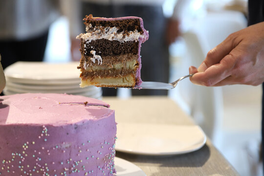 Hand serving slice of layered chocolate birthday cake with purple frosting