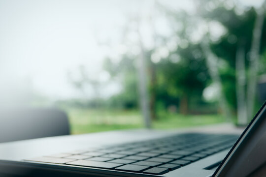 Close up of laptop keyboard on a wooden table with blurred green nature background, concept of remote work, remote learning, and freelance lifestyle in an outdoor setting.