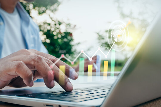Man typing on laptop with digital business growth chart and 2027 target overlay in outdoor nature setting, concept of corporate success, strategic planning, and future vision.